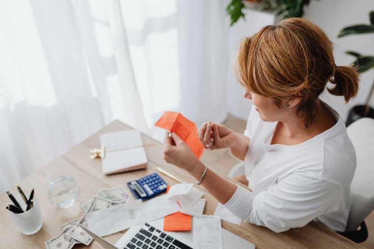 A person checking their finances with a laptop and paperwork at home