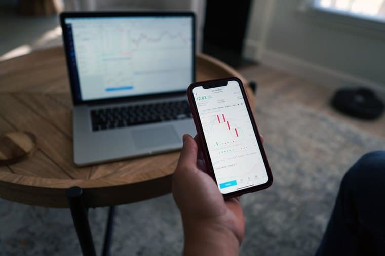 A person reviewing investment charts on a phone and laptop
