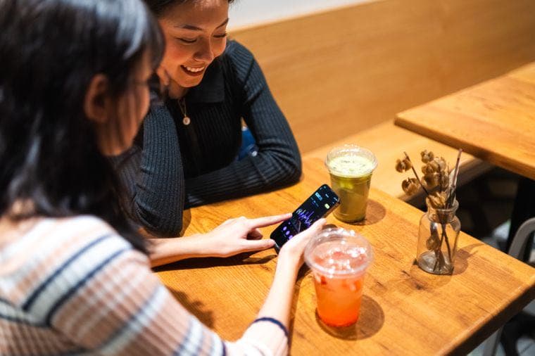 Two young women looking at a finance app on a phone in a cafe