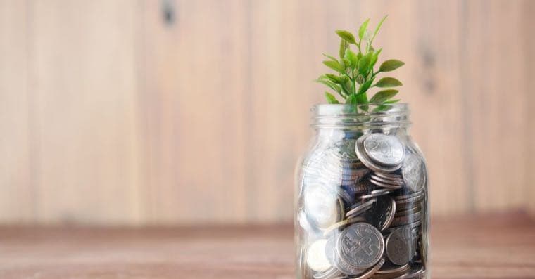 A glass jar of coins with a small plant growing, symbolising savings growth